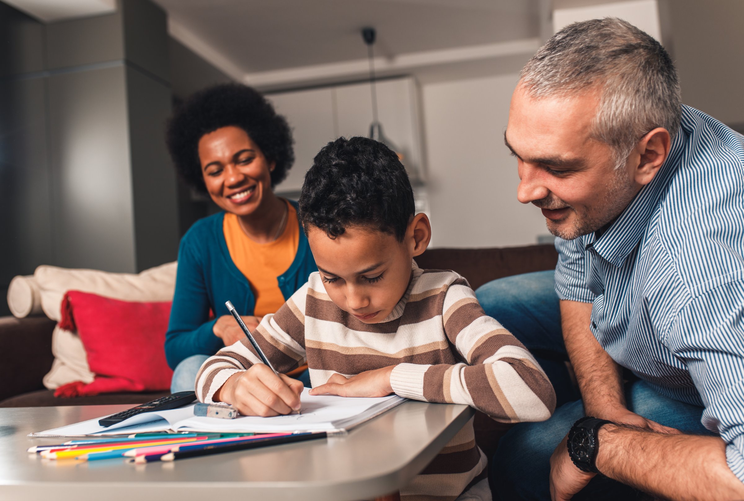 Two parents helping a boy with his homework at the kitchen table
