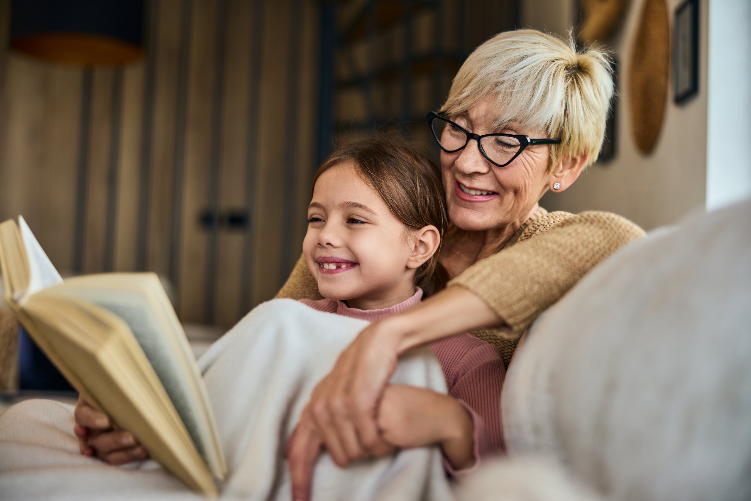 A grandmother reading a book with her grandchild on the couch
