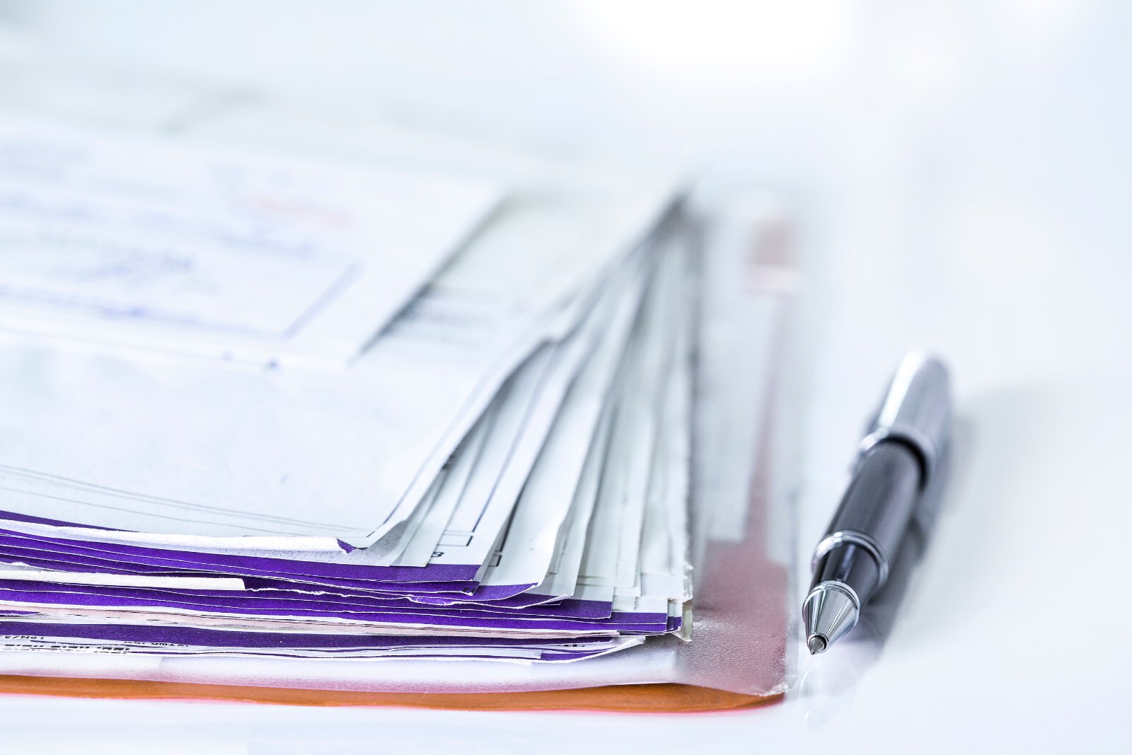 A stack of bills and a pen on a desk