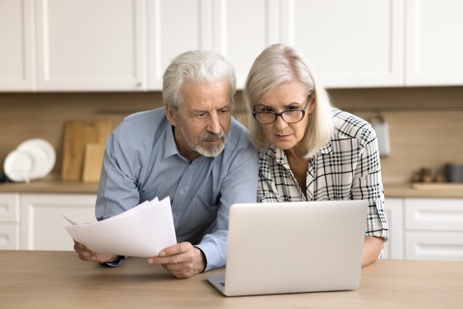A couple reviews paper statements and a laptop at their kitchen table